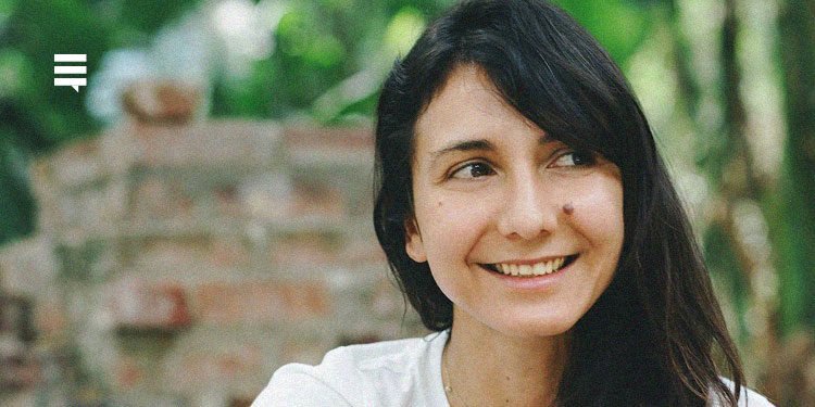 A escritora Ottessa Moshfegh. Ela sorri, olhando para o lado direito. Ela usa camiseta branca, cabelo solto e está ao ar livre.