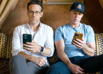 Ryan Reynolds e Rob McElhenney sentados em um sofá mexendo no celular.