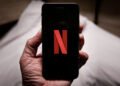Mão segurando celular conectado no aplicativo da Netflix